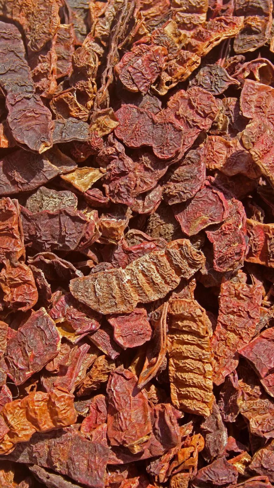 Close-up of dried shikakai pods broken into small reddish-brown pieces, showing their wrinkled texture.